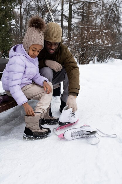 Young girl putting on her ice skates with the help of her father