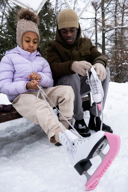 Young girl putting on her ice skates with the help of her father