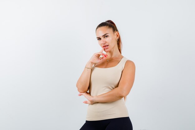 Young girl putting index finger near mouth, holding hand under elbow in beige top