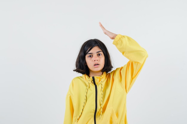 Молодая девушка поднимает руку над головой в желтой куртке-бомбардировщике и выглядит серьезно.