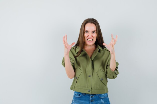 Young girl raising hands in aggressive manner in jacket, shorts front view.