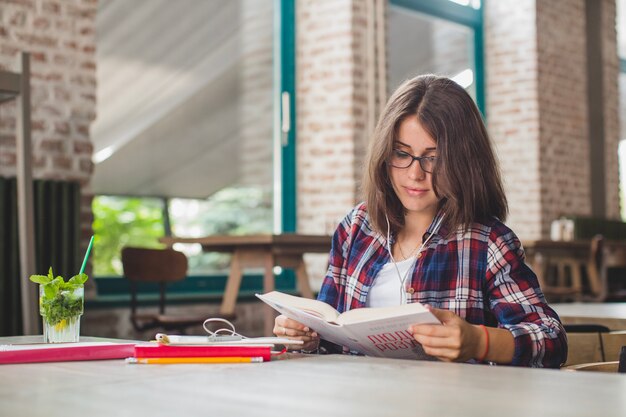 Молодая девушка, читающая книгу в наушниках