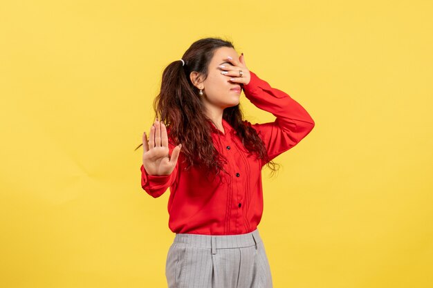 young girl in red blouse covering her face on yellow