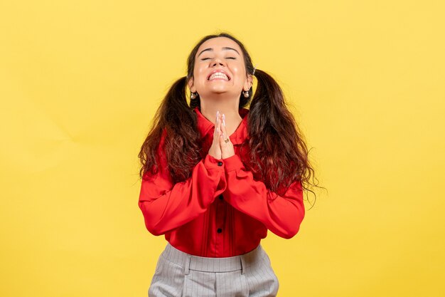 young girl in red blouse posing and praying on yellow
