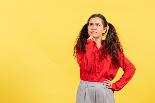 young girl in red blouse posing and thinking on yellow