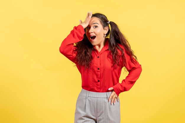 young girl in red blouse posing with excited face on yellow