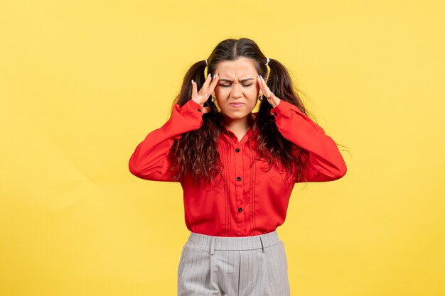 young girl in red blouse posing with painful face on yellow