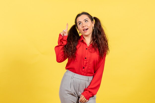 young girl in red blouse raising her finger on yellow