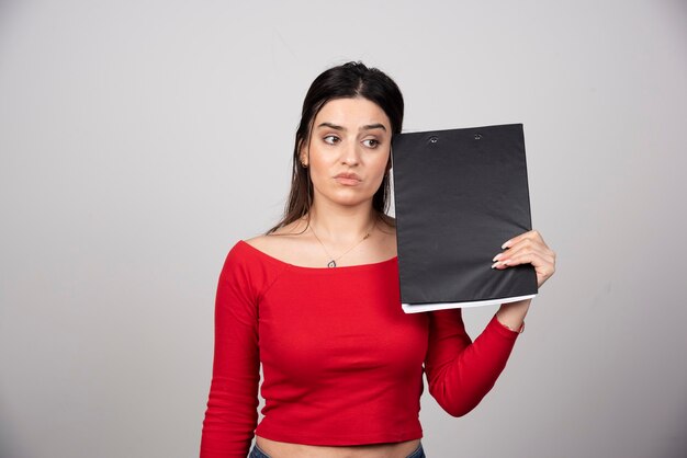 Young girl in red blouse with clipboard thinking about something.