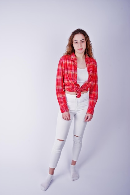 Giovane ragazza in camicia a quadri rossa e pantaloni bianchi su sfondo bianco in studio