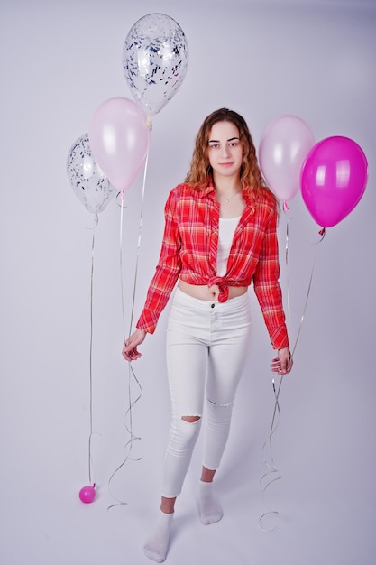 Young girl in red checked shirt and white pants with balloons against white background on studio