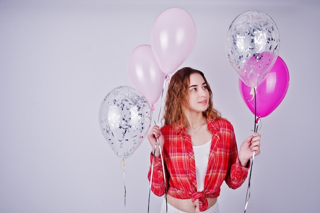 Young girl in red checked shirt and white pants with balloons against white background on studio