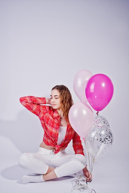 Young girl in red checked shirt and white pants with balloons against white background on studio