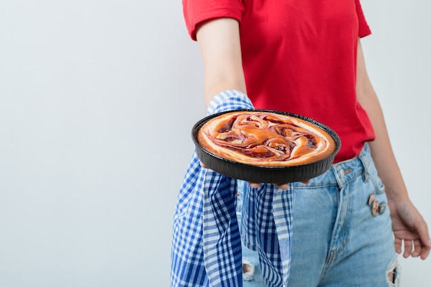 Молодая девушка в красной рубашке держит пирог на черной сковороде