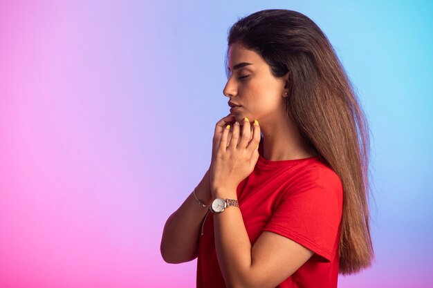 Young girl in red shirt touching her face.