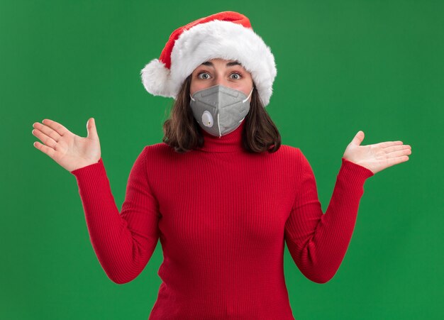Young girl in red sweater and santa hat wearing facial protective mask looking at camera happy and cheerful