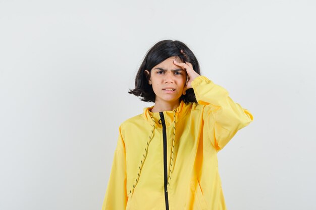 Young girl scratching head, thinking about something in yellow bomber jacket and looking pensive.