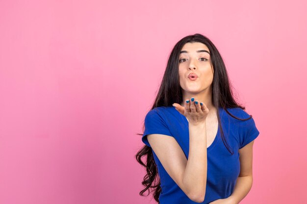 Young girl sending kiss to the camera on pink background High quality photo