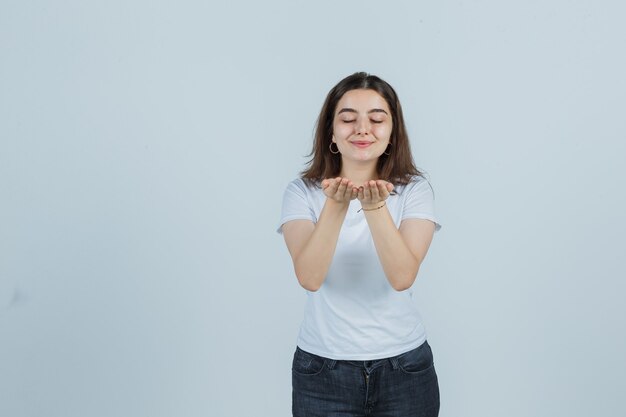 Young girl sending kiss with hands in t-shirt, jeans and looking pretty. front view.