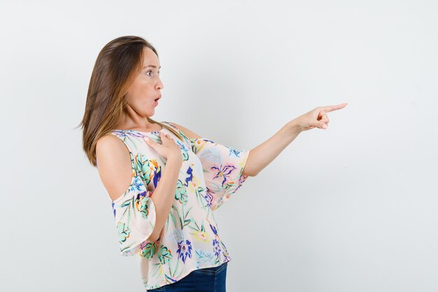 Young girl in shirt, jeans pointing to side and looking scared , front view.