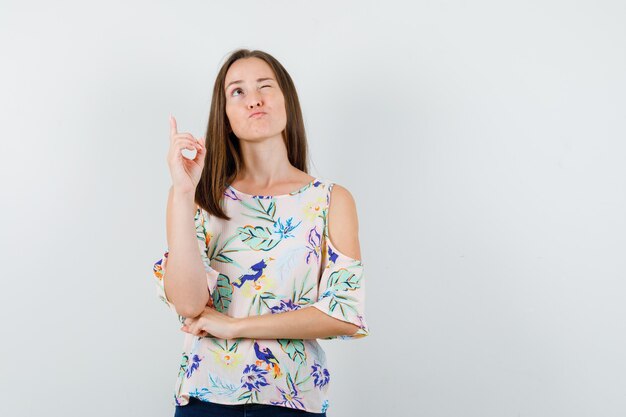 Young girl in shirt, jeans pointing up and looking pensive , front view.