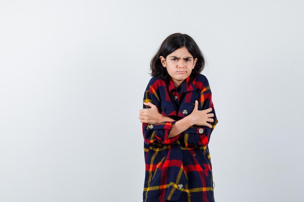 Young girl shivering from cold in checked shirt and looking annoyed. front view.