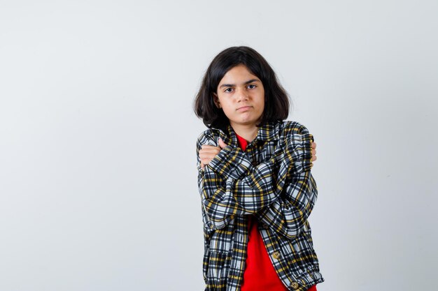 Young girl shivering from cold in checked shirt and red t-shirt and looking serious. front view.