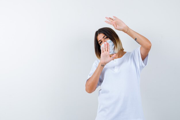 Young girl showing four fingers gesture and stop sign in white t-shirt and mask and looking confident , front view.