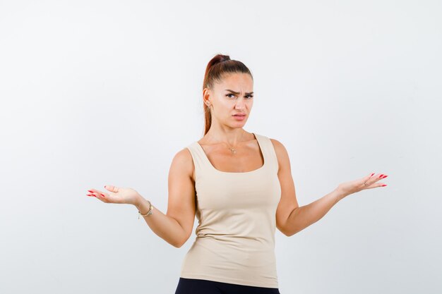 Young girl showing helpless gesture in beige top, black pants and looking puzzled