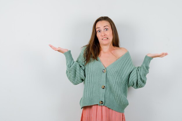 Young girl showing helpless gesture in knitwear, skirt and looking puzzled. front view.