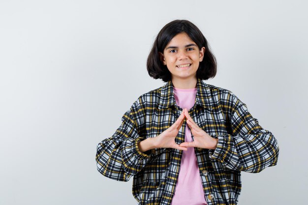 Young girl showing insurance gesture in checked shirt and pink t-shirt and looking cute , front view.