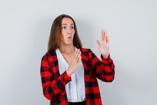 Young girl showing karate chop gesture in checkered shirt, blouse and looking surprised , front view.