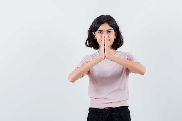 Young girl showing namaste gesture in pink t-shirt and black pants and looking happy