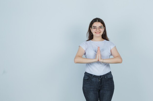 Tシャツ、ジーンズでナマステのジェスチャーを示し、幸せそうに見える若い女の子、正面図。