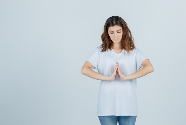 Young girl showing namaste gesture in white t-shirt and looking calm , front view.