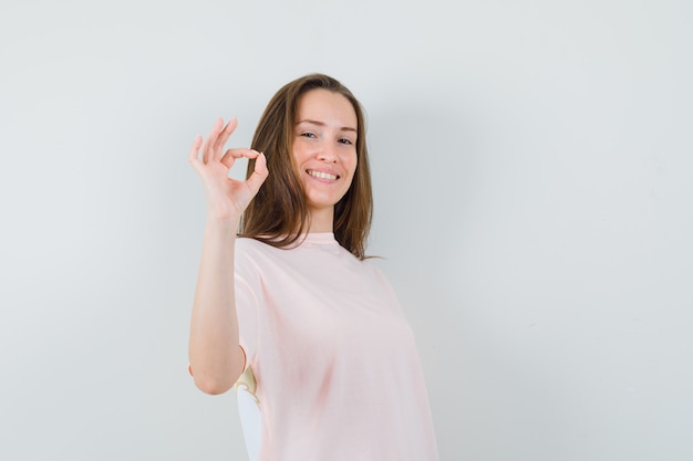 Young girl showing ok gesture in pink t-shirt and looking cheery , front view.