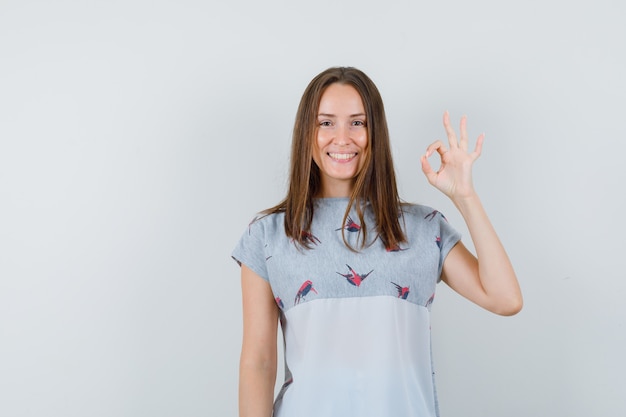 Young girl showing ok gesture in t-shirt and looking cheery. front view.