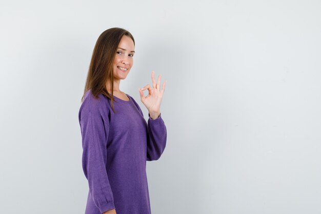 Young girl showing ok gesture in violet shirt and looking jolly , front view.
