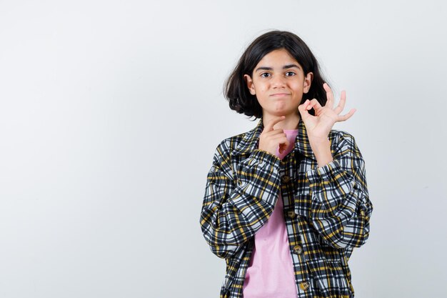 チェックシャツとピンクのTシャツでOKサインを見せて、きれいに見える若い女の子、正面図。