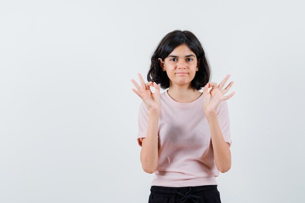 Young girl showing ok sign with both hands in pink t-shirt and black pants and looking happy