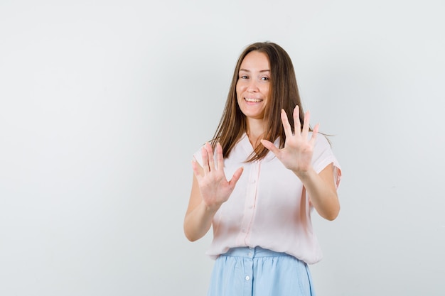 Young girl showing refusal gesture in t-shirt, skirt and looking optimistic , front view.