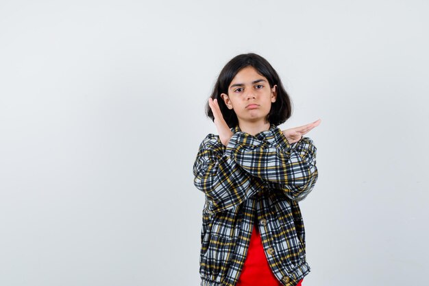 チェックのシャツと赤いTシャツで制限ジェスチャーを示し、キュートに見える少女、正面図。