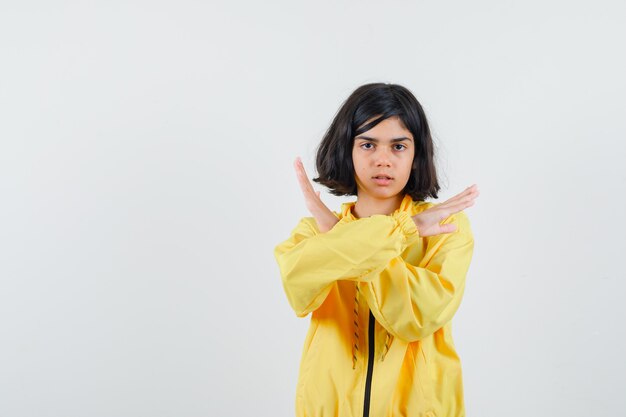 Young girl showing restriction gesture with crossed hands in yellow bomber jacket and looking serious