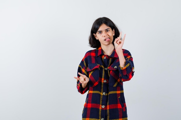 Young girl showing rock n roll gestures, sticking tongue out in checked shirt and looking cute. front view.