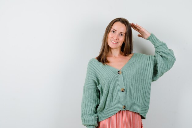 Young girl showing salute gesture in knitwear, skirt and looking cheery , front view.