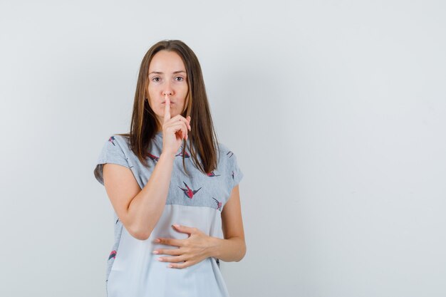 Young girl showing silence gesture in t-shirt and looking careful. front view.