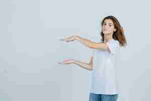 Free photo young girl showing size sign in t-shirt, jeans and looking confident , front view.