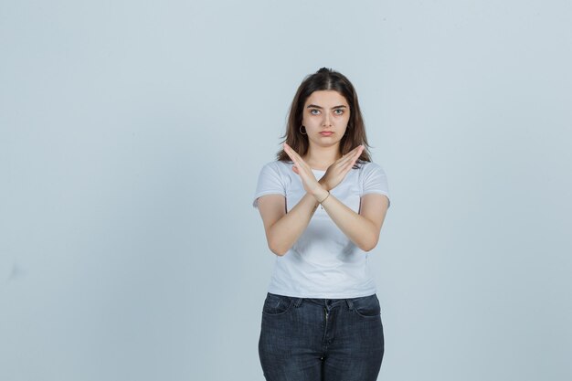 Молодая девушка показывает жест стоп в футболке, джинсах и выглядит серьезно. передний план.