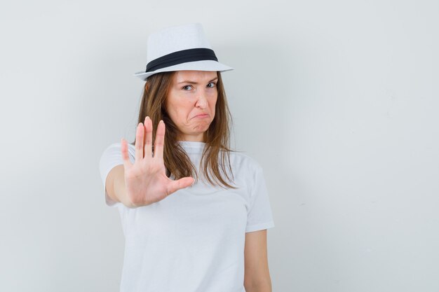 Young girl showing stop gesture in white t-shirt hat and looking annoyed 