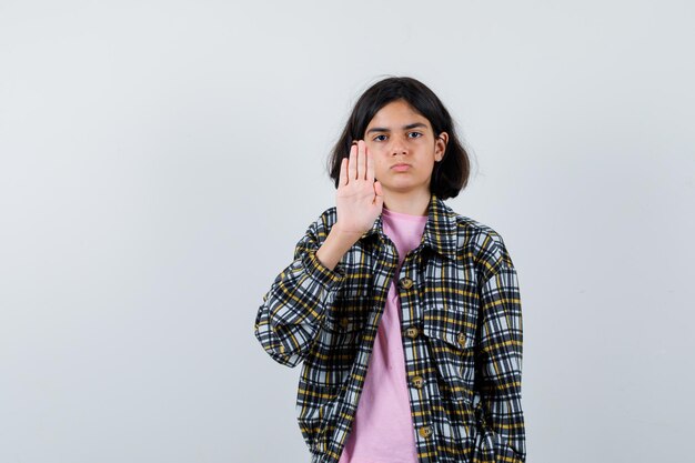 チェックシャツとピンクのtシャツで一時停止の標識を示し、真剣に見える少女。正面図。